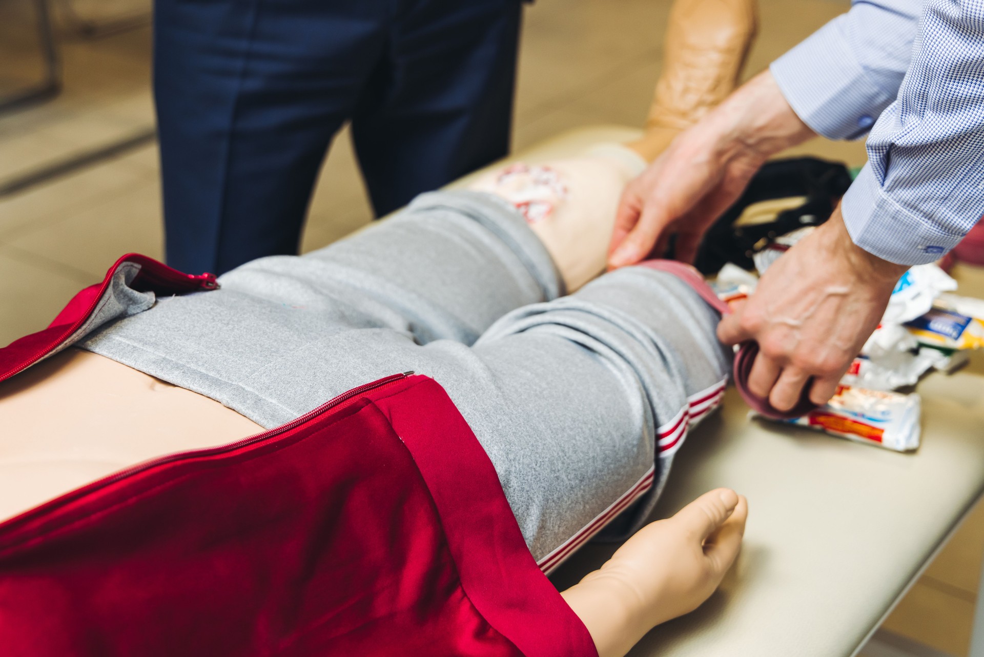 First aid training course with dummy, CPR emergency reanimation procedure on mannequin, instructor demonstrating medical training with doll, chest compression and applying bandage and tourniquet